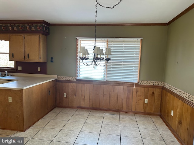 kitchen featuring hanging light fixtures, wooden walls, light tile patterned floors, kitchen peninsula, and a chandelier