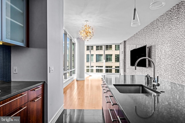 kitchen with dark stone counters, an inviting chandelier, sink, hanging light fixtures, and light wood-type flooring