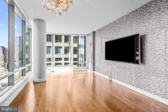 unfurnished living room featuring wood-type flooring, ornate columns, a wall of windows, and a notable chandelier