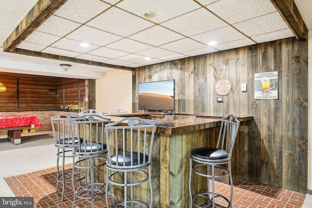 bar featuring dark colored carpet, a paneled ceiling, and wood walls