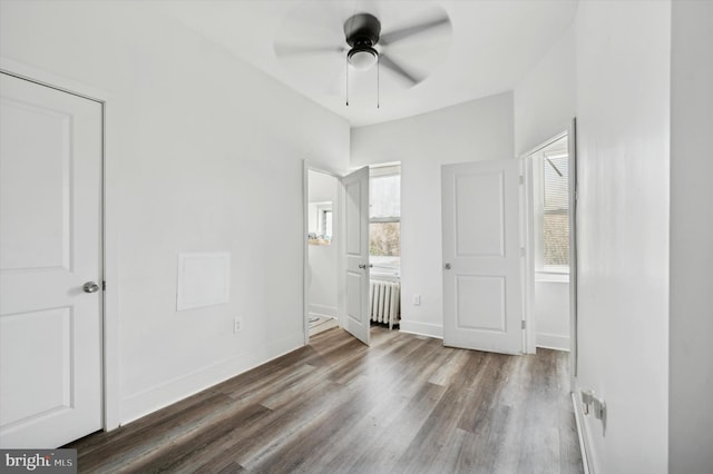 unfurnished bedroom with ceiling fan, dark wood-type flooring, radiator, and multiple windows