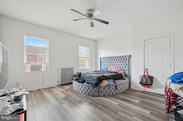 bedroom featuring multiple windows, ceiling fan, radiator heating unit, and light hardwood / wood-style flooring