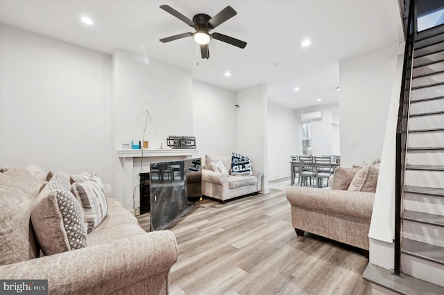 living room with a wall mounted air conditioner, light hardwood / wood-style flooring, and ceiling fan