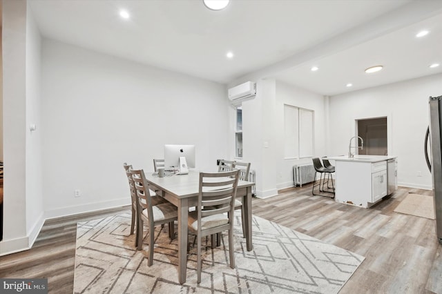 dining area featuring a wall unit AC, radiator, sink, and light hardwood / wood-style floors