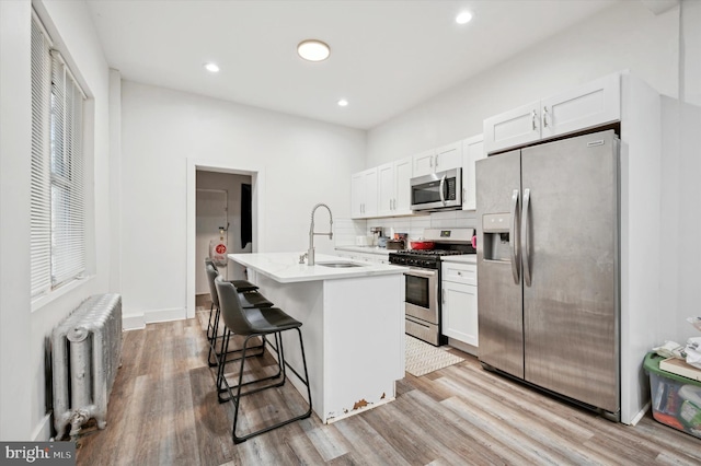 kitchen with radiator, a center island with sink, a kitchen breakfast bar, white cabinets, and stainless steel appliances