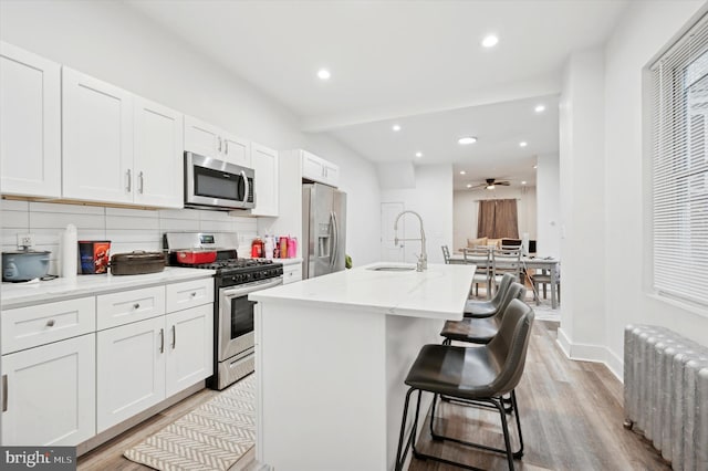 kitchen featuring a center island with sink, sink, appliances with stainless steel finishes, radiator heating unit, and a breakfast bar area