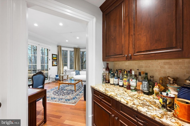 bar featuring light stone counters, decorative backsplash, light hardwood / wood-style floors, and crown molding