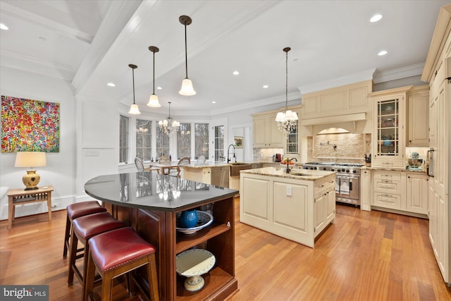 kitchen featuring appliances with stainless steel finishes, a kitchen bar, a kitchen island with sink, an inviting chandelier, and cream cabinetry