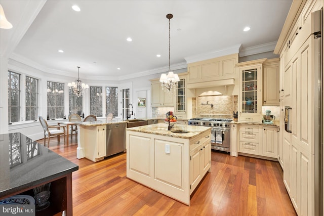 kitchen featuring appliances with stainless steel finishes, decorative light fixtures, a kitchen island with sink, a notable chandelier, and cream cabinetry