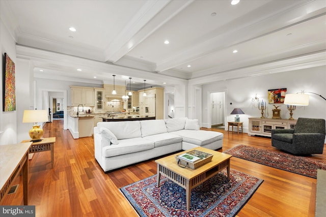 living room featuring ornamental molding, sink, beam ceiling, and light hardwood / wood-style flooring