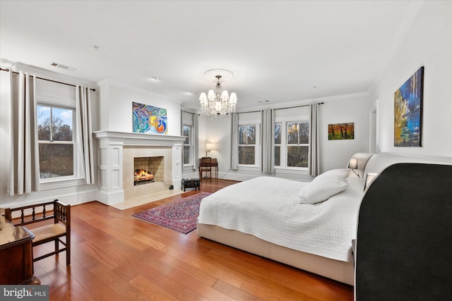 bedroom with crown molding, a premium fireplace, hardwood / wood-style floors, and a notable chandelier