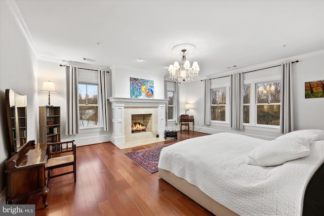 bedroom with crown molding, wood-type flooring, a fireplace, and a chandelier