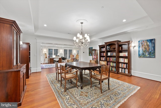 dining area featuring an inviting chandelier, a raised ceiling, and light hardwood / wood-style flooring