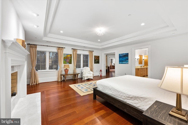 bedroom featuring hardwood / wood-style floors, ensuite bathroom, a fireplace, ornamental molding, and a raised ceiling