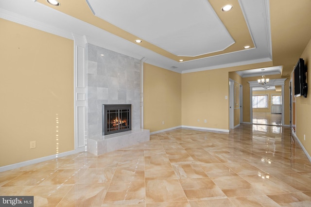 unfurnished living room with a fireplace, a tray ceiling, crown molding, and a notable chandelier