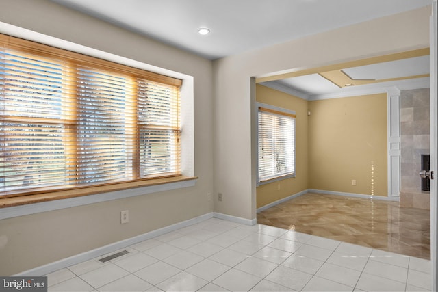 spare room featuring light tile patterned floors, ornamental molding, a fireplace, and a wealth of natural light