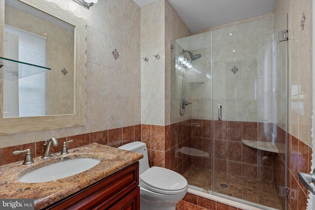 bathroom with vanity, a shower with door, toilet, and tile walls