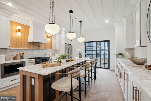 kitchen featuring light stone counters, white cabinetry, a kitchen island with sink, and custom range hood