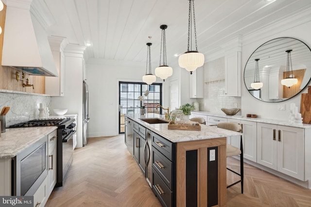 kitchen featuring white cabinets, sink, a center island with sink, and premium range hood