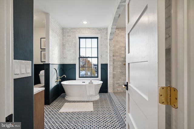 bathroom featuring vanity, a tub to relax in, toilet, and tile walls