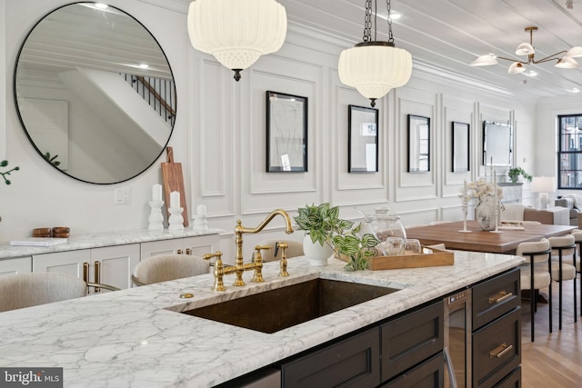 kitchen featuring light stone countertops, sink, crown molding, light hardwood / wood-style floors, and decorative light fixtures