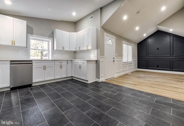 kitchen with stainless steel dishwasher, vaulted ceiling, sink, and white cabinetry