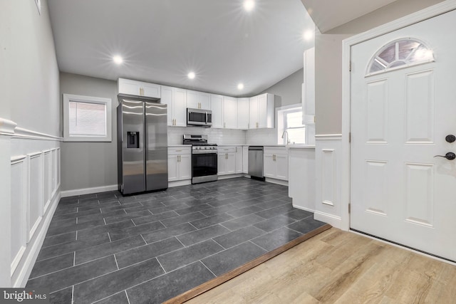 kitchen with tasteful backsplash, vaulted ceiling, sink, appliances with stainless steel finishes, and white cabinets