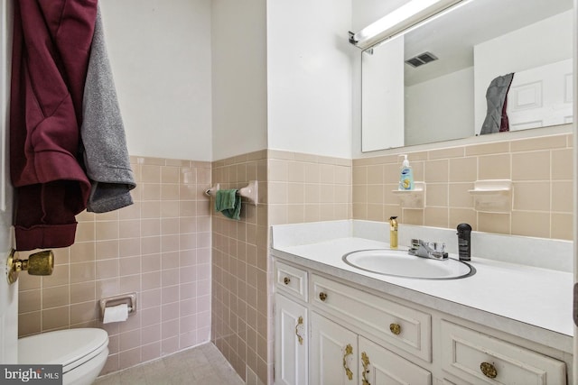 bathroom featuring tile patterned flooring, vanity, toilet, and tile walls