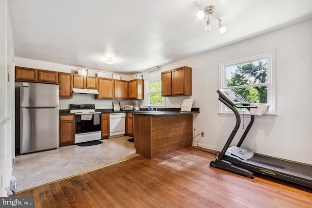 kitchen with light wood-type flooring, white appliances, kitchen peninsula, and a healthy amount of sunlight