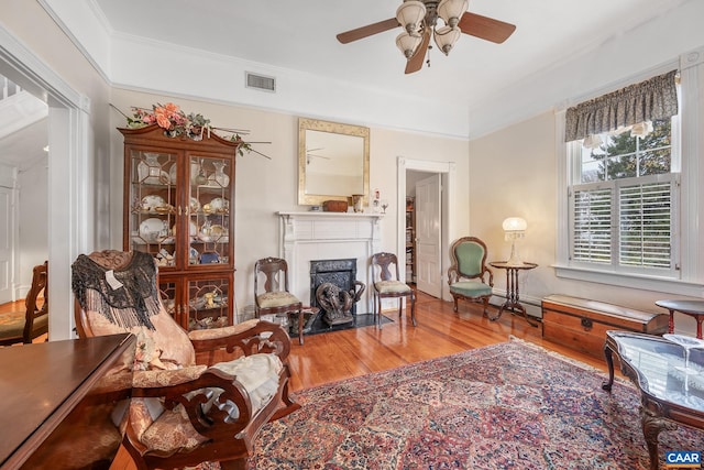 living area featuring wood-type flooring, ceiling fan, and ornamental molding