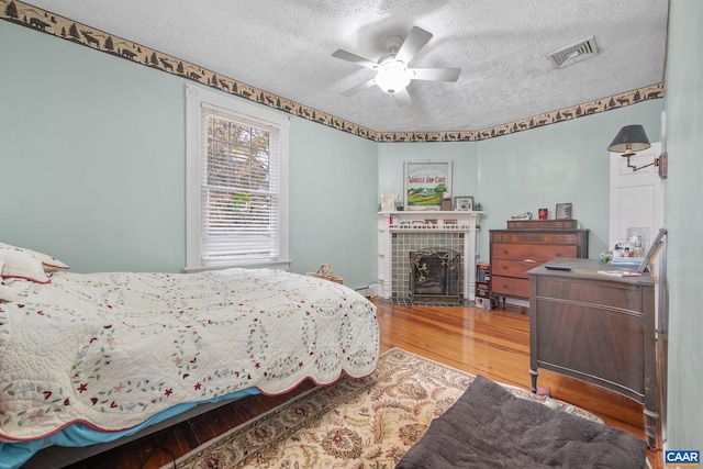 bedroom featuring hardwood / wood-style flooring, ceiling fan, a textured ceiling, and a tile fireplace