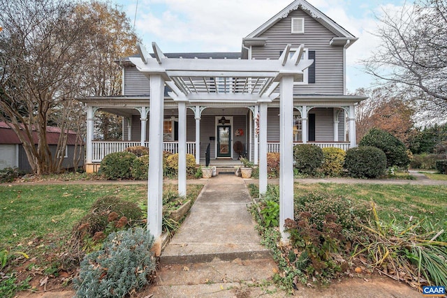 view of property featuring covered porch, a pergola, and a front yard