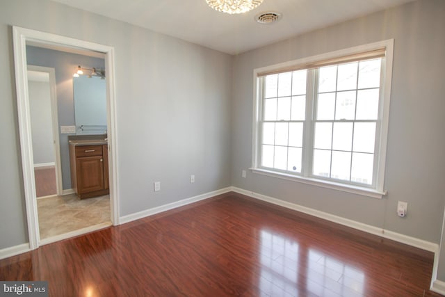 empty room featuring a notable chandelier, a healthy amount of sunlight, and dark wood-type flooring