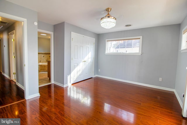 unfurnished bedroom with ensuite bath, a closet, dark wood-type flooring, and a notable chandelier