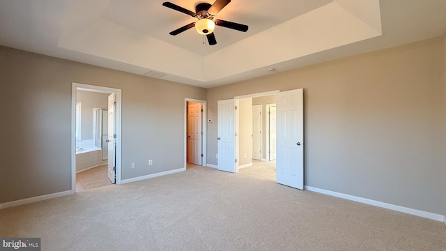 unfurnished bedroom with ensuite bath, a raised ceiling, and light colored carpet