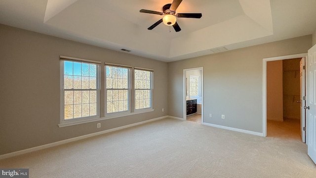 unfurnished bedroom with a tray ceiling, ceiling fan, light carpet, and ensuite bathroom