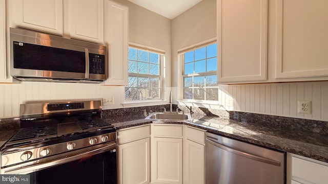 kitchen featuring white cabinets, appliances with stainless steel finishes, and dark stone counters