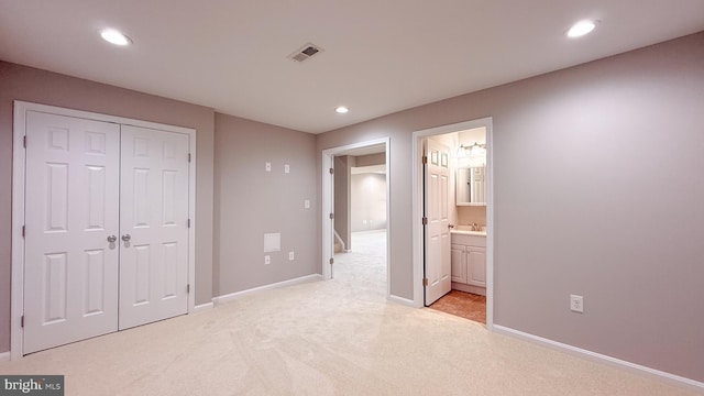 unfurnished bedroom with light carpet, a closet, ensuite bath, and sink