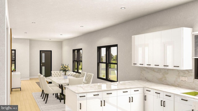 kitchen featuring white cabinetry, decorative backsplash, kitchen peninsula, and light stone counters