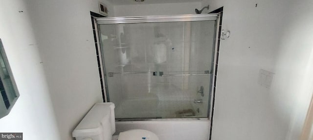 bathroom featuring toilet and bath / shower combo with glass door