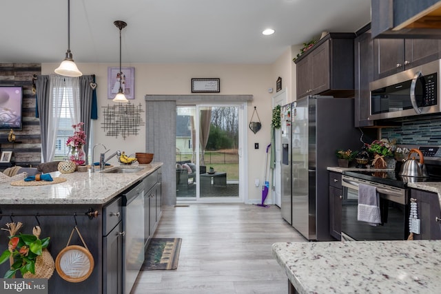 kitchen with dark brown cabinetry, light stone countertops, decorative light fixtures, appliances with stainless steel finishes, and light wood-type flooring