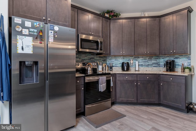 kitchen featuring backsplash, light stone counters, dark brown cabinets, stainless steel appliances, and light hardwood / wood-style flooring