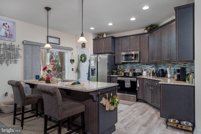 kitchen featuring light stone countertops, stainless steel appliances, decorative light fixtures, light hardwood / wood-style floors, and an island with sink