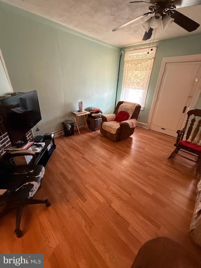 interior space featuring ceiling fan, wood walls, light wood-type flooring, and a textured ceiling