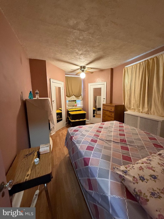 bedroom with ceiling fan, radiator heating unit, a textured ceiling, and hardwood / wood-style flooring