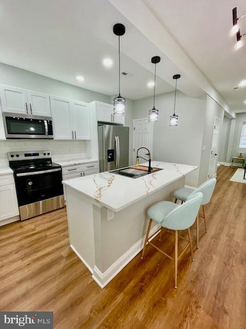 kitchen featuring white cabinets, a kitchen island with sink, sink, and appliances with stainless steel finishes