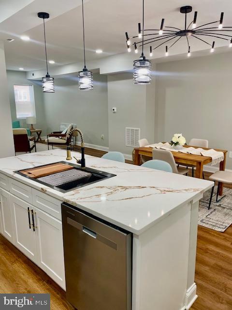 kitchen with sink, hanging light fixtures, stainless steel dishwasher, wood-type flooring, and white cabinets