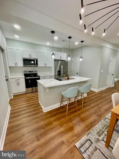 kitchen featuring appliances with stainless steel finishes, light wood-type flooring, a kitchen island with sink, white cabinetry, and hanging light fixtures