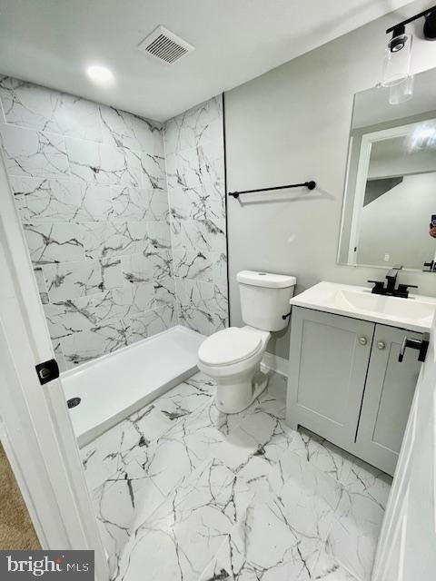 bathroom featuring vanity, toilet, and tiled shower