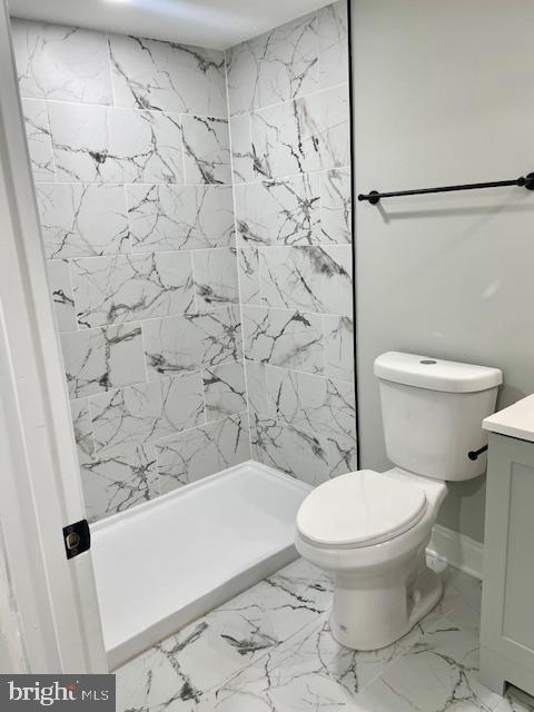 bathroom with tiled shower, vanity, and toilet